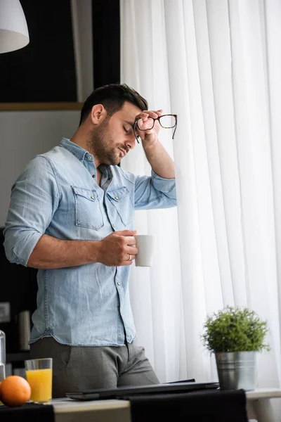 stock image handsome guy is drinking coffee, standing near window 