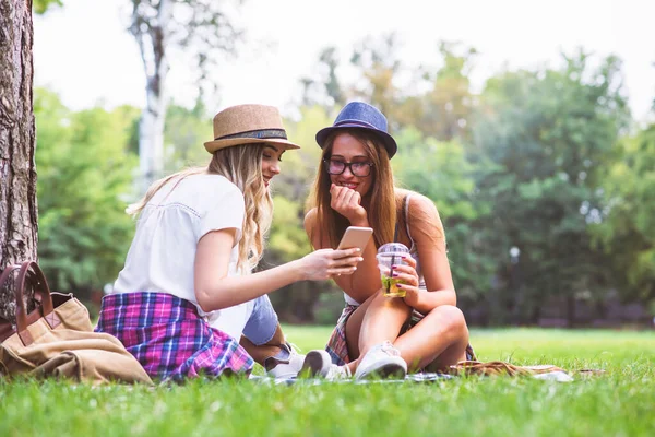2人の女性の友人が草の上に座って電話をし — ストック写真