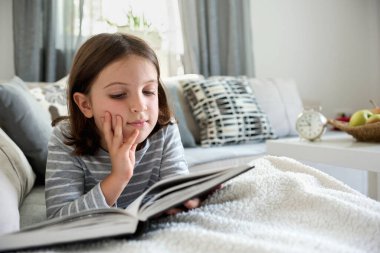 Kanepede kitap okuyan güzel küçük bir kız. 