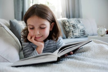 Kanepede kitap okuyan güzel küçük bir kız. 