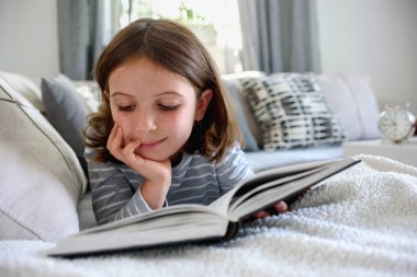 Kanepede kitap okuyan güzel küçük bir kız. 