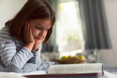 Kanepede kitap okuyan güzel küçük bir kız. 