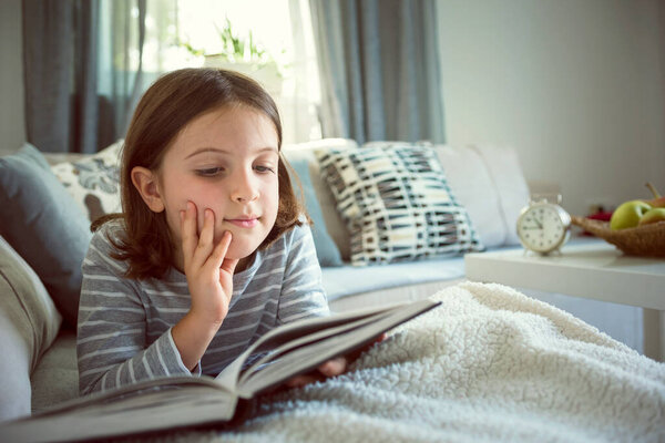 beautiful little girl reading book on sofa 