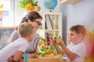 Anaokulunda renkli ahşap oyuncaklarla oynayan çocuklu anaokulu öğretmeni.