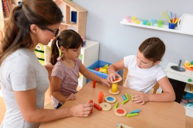 Anaokulunda renkli ahşap oyuncaklarla oynayan çocuklu anaokulu öğretmeni.