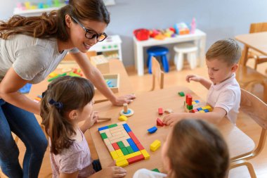 Anaokulunda renkli ahşap oyuncaklarla oynayan çocuklu anaokulu öğretmeni.