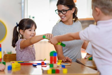 Anaokulunda renkli ahşap oyuncaklarla oynayan çocuklu anaokulu öğretmeni.