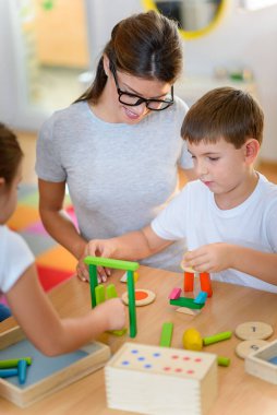 Anaokulunda renkli ahşap oyuncaklarla oynayan çocuklu anaokulu öğretmeni.