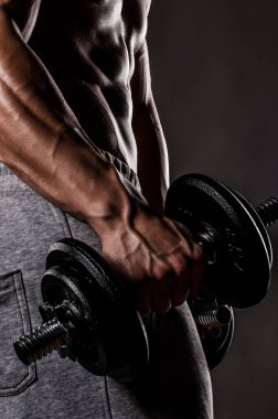 Çıplak gövdeli kaslı bir adam siyah arka planda izole haldeki dambılları tutuyor.