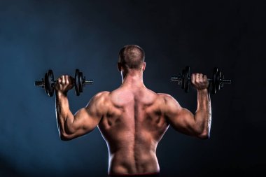 Siyah arka planda dambılları olan kaslı adam. 