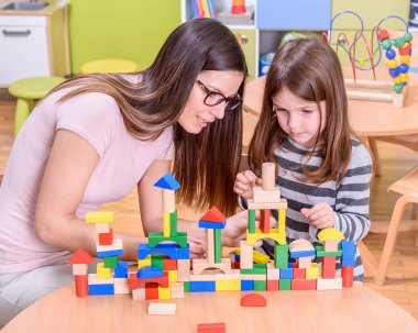 Öğretmen ve kız okulda oyuncak bloklarıyla oynuyor.