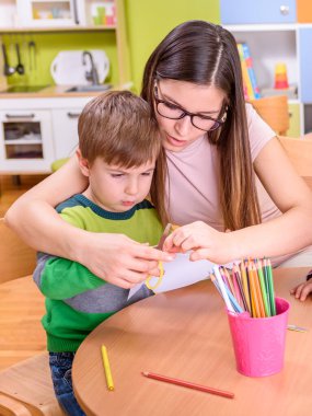 Anaokulu öğretmeni kesim ve çizim konusunda bir çocuğa yardım ediyor.