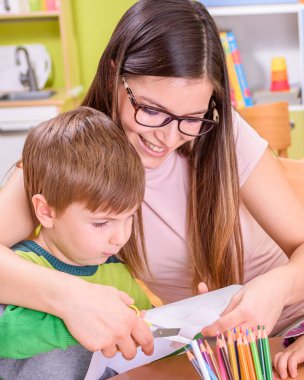 Anaokulu öğretmeni kesim ve çizim konusunda bir çocuğa yardım ediyor.