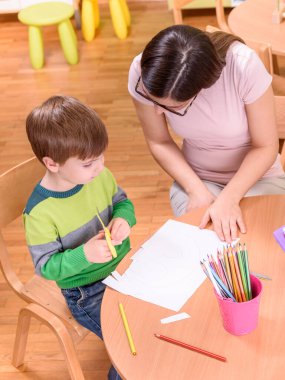 Anaokulu öğretmeni kesim ve çizim konusunda bir çocuğa yardım ediyor.