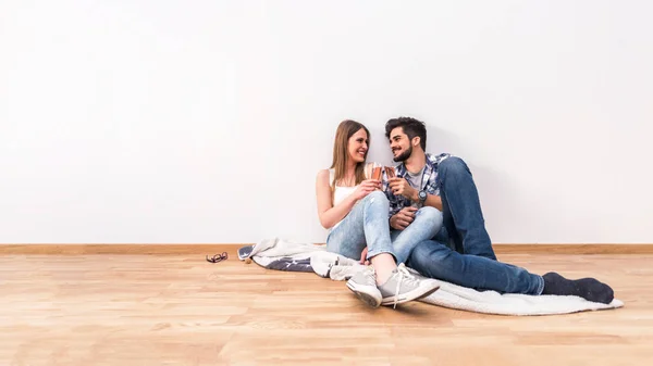 一对年轻夫妇坐在空荡荡的公寓地板上 用香槟庆祝 — 图库照片