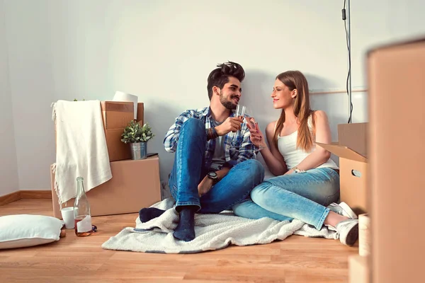 一对年轻夫妇坐在空荡荡的公寓地板上 用香槟庆祝 — 图库照片