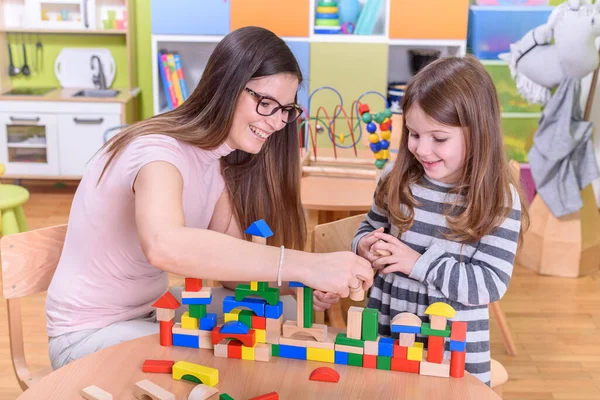 teacher and girl playing with toy blocks at school