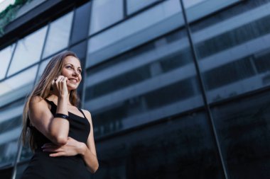 Akıllı telefondan konuşan güzel kız, şehir binasının yanında duruyor.