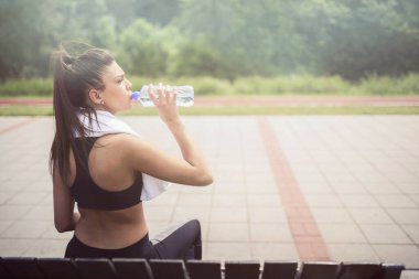 Spor kızı bankta oturuyor, su içiyor.