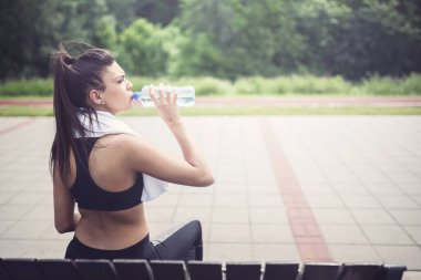 Spor kızı bankta oturuyor, su içiyor.