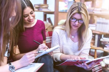 Bir grup genç kız üniversite öğrencisi kütüphanede birlikte okuyorlar.