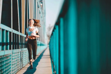 Şehirdeki köprüde koşan taytlı genç bayan koşucu.