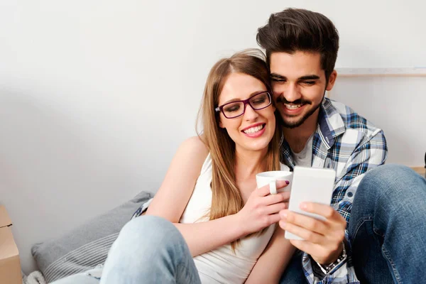 一对年轻夫妇坐在空荡荡的公寓地板上 看着智能手机 搬到新家去 — 图库照片