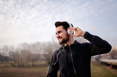 Sabah egzersizi yapan adam ara verip müzik dinliyor.