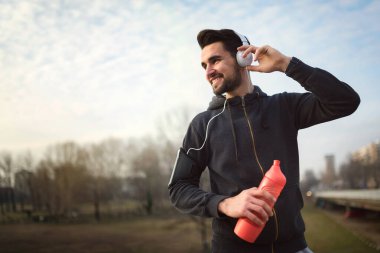 Sabah egzersizi yapan adam ara verip müzik dinliyor.