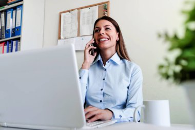 Ofisteki iş kadını bilgisayarla telefonda konuşuyor.