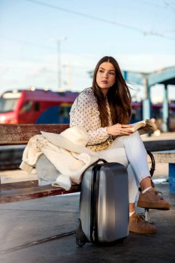 Tren istasyonundaki bavullu kız, kitap okuyor.
