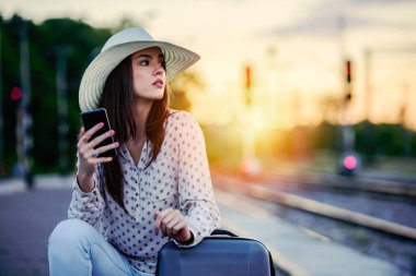 Tren istasyonunda bavulu ve telefonu olan genç bir kadın.