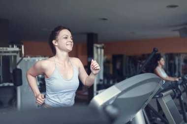 Spor kıyafetli güzel bir fitness salonu koşu bandında koşan genç bir kadın. Spor salonundaki güzel kız..