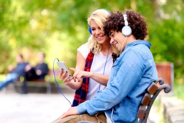 Kulaklıklı genç çift dışarıda akıllı telefon kullanarak müzik dinliyor.