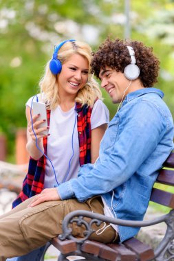 Kulaklıklı genç çift dışarıda akıllı telefon kullanarak müzik dinliyor.