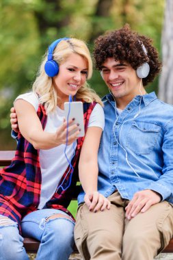 Kulaklıklı genç çift dışarıda akıllı telefon kullanarak müzik dinliyor.