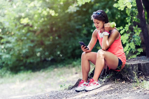 Aktif spor kızı parkta oturmuş elma yiyor ve müzik dinliyor.