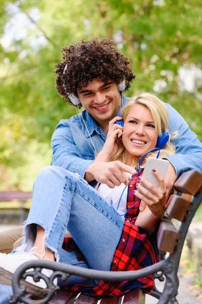 带耳机的年轻夫妇在户外用智能手机听音乐 — 图库照片
