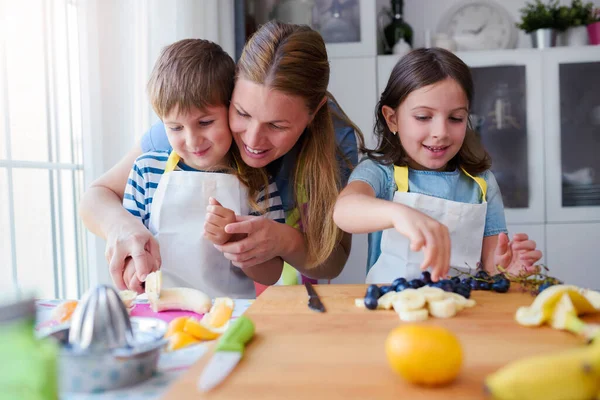キッチンで母親と一緒に幸せな若い子供たち 健康的なフルーツスナックを準備する — ストック写真