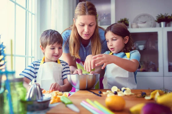 Happy young kids with their mother in the kitchen - preparing a healthy fruits snacks