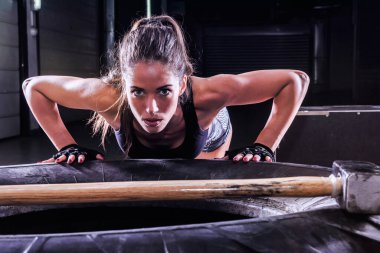 Spor salonunda çekiçle lastik üzerinde poz veren çekici, fit bir kadın.