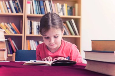 Küçük kız kütüphanede kitap okuyor. 
