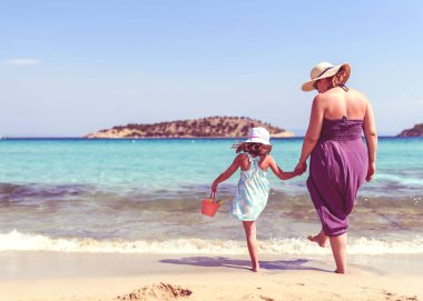 Mükemmel zümrüt plajında duran bir anne ve kızın arka görüntüsü.