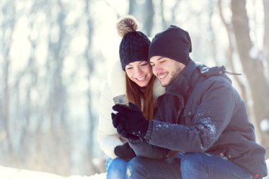 Kar altında gülümseyen genç bir çift akıllı telefona bakıyordu.