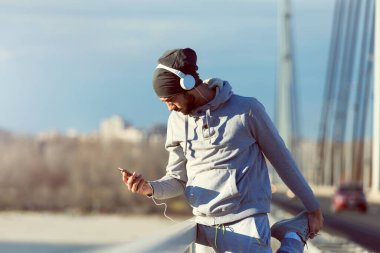 Erkek koşucu yoğun bir eğitimden sonra cep telefonundan müzik dinliyor. 