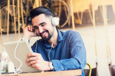 Kulaklıklı genç adam kafede tablet kullanarak oturuyor.