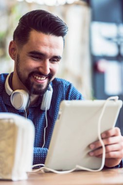 Kulaklıklı genç adam kafede tablet kullanarak oturuyor.