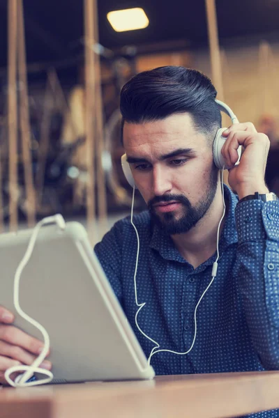 stock image young man with headphones sitting at table in cafe using tablet