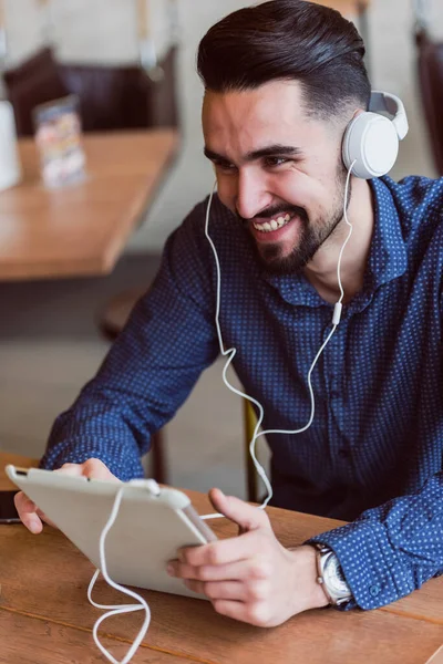 Stock image young man with headphones sitting at table in cafe using tablet