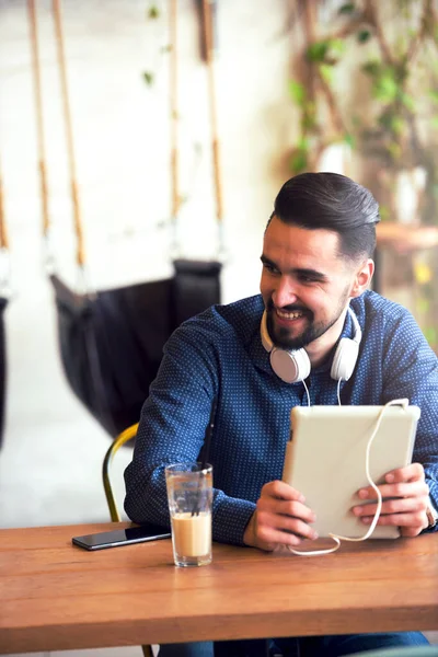 Kulaklıklı genç adam kafede tablet kullanarak oturuyor.